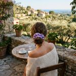Woman with lavender scrunchie in hair bun and off-shoulder cream sweater at cafe